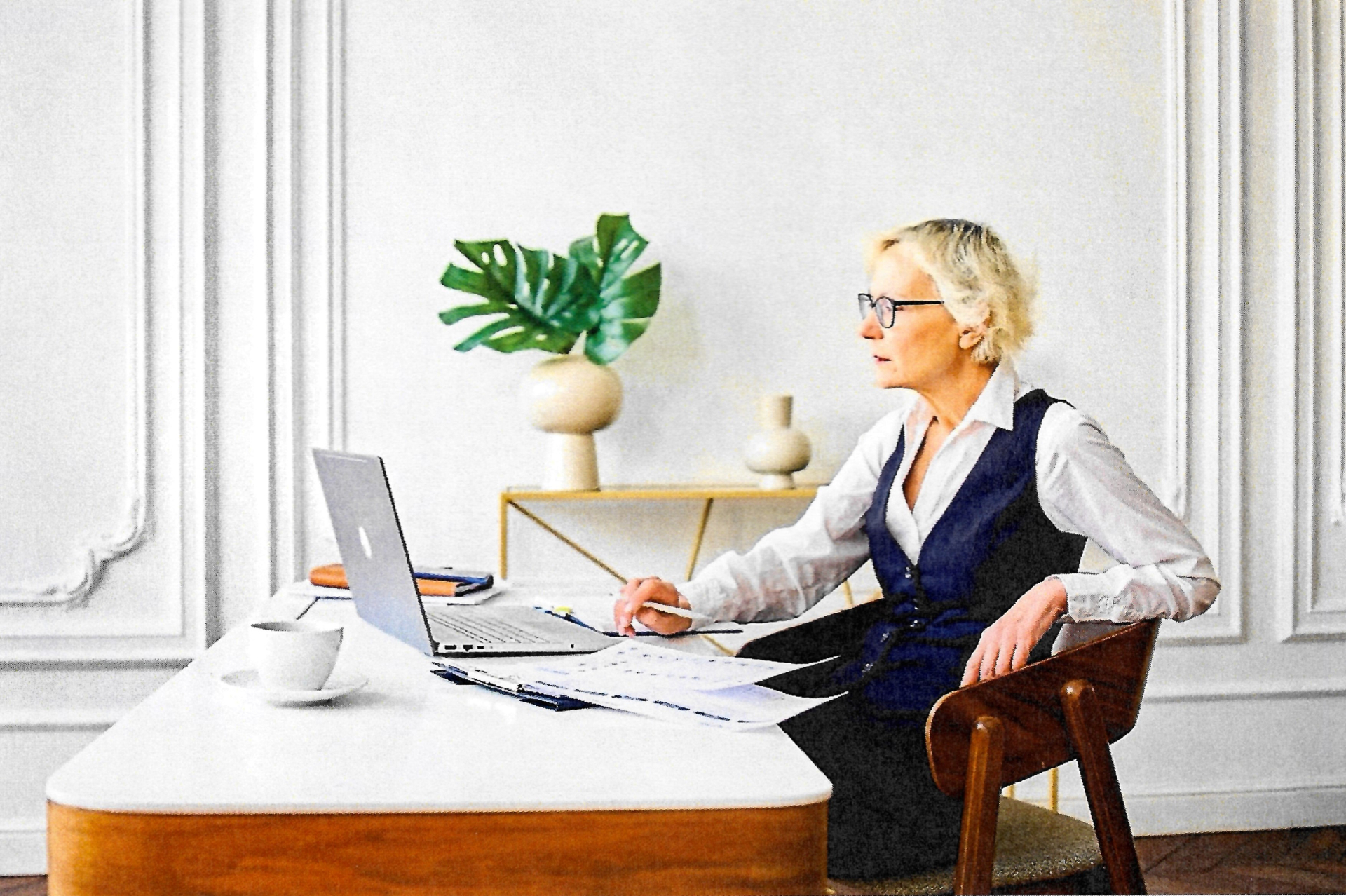 Paula Conner working at her desk with a laptop and printed drafts